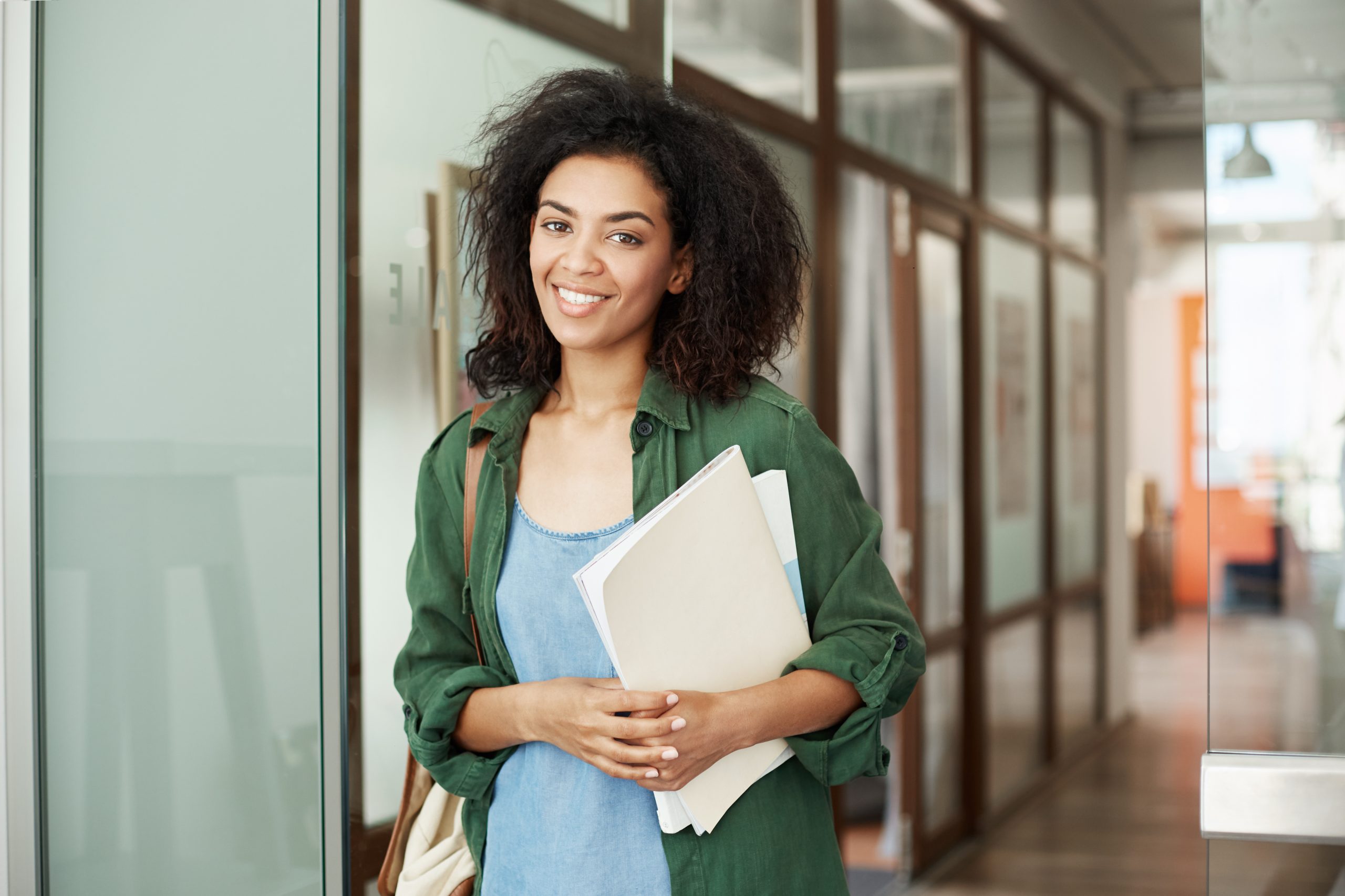 Cheerful african beautiful girl student smiling looking at camera holding books in university. Education concept.